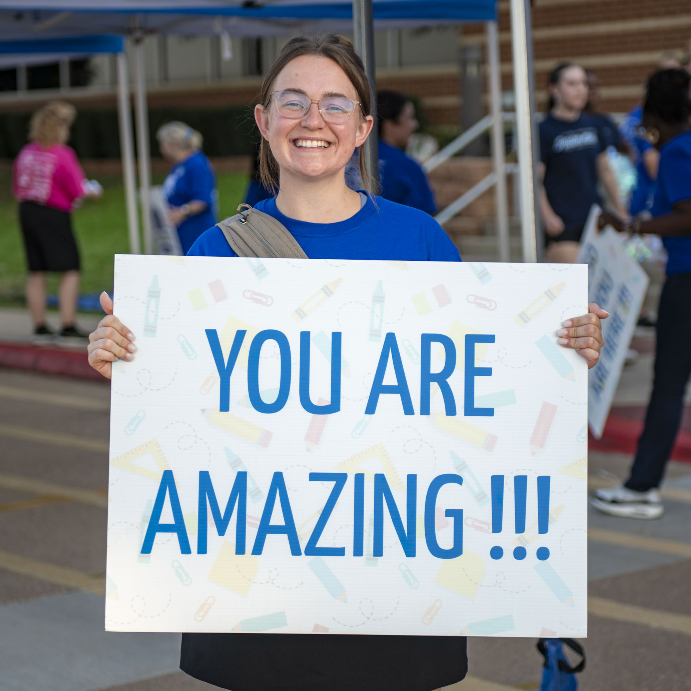Volunteer welcomes families with an encouraging sign at Operation Back 2 School.