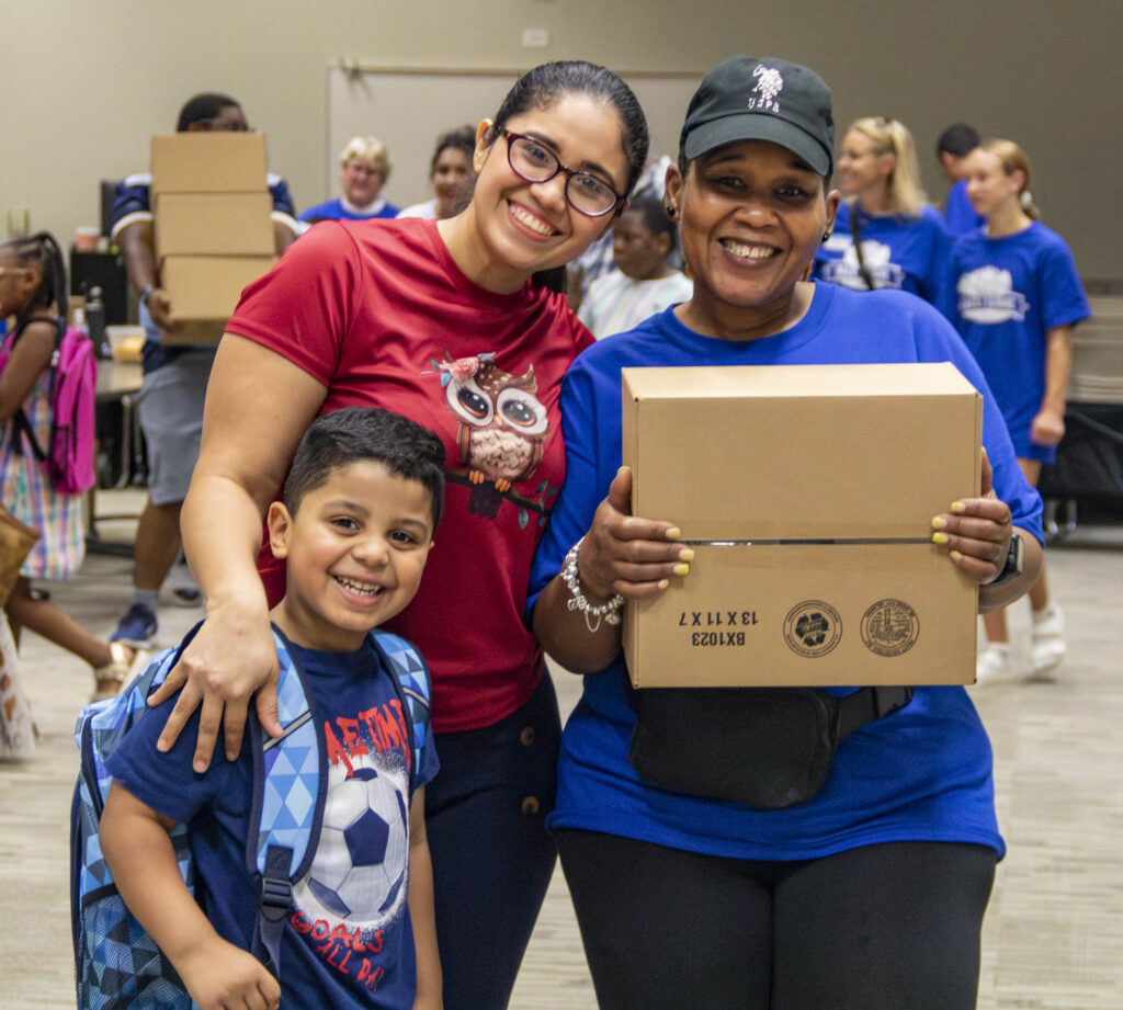 Volunteer stands with a family receiving supplies at Operation Back 2 School.