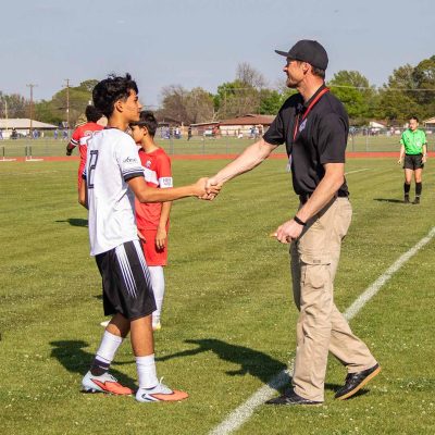 Liga HEB soccer volunteer shakes hands with a junior high player on the field